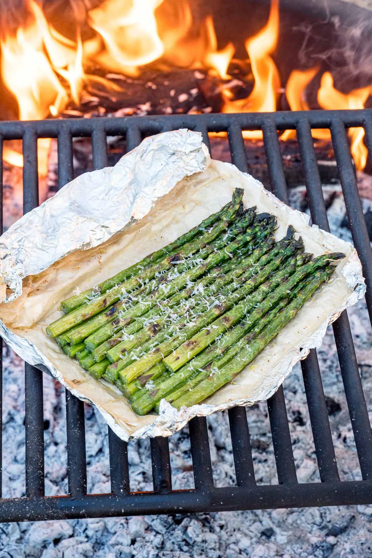 Grilled asparagus foil packets with open flame in the background.