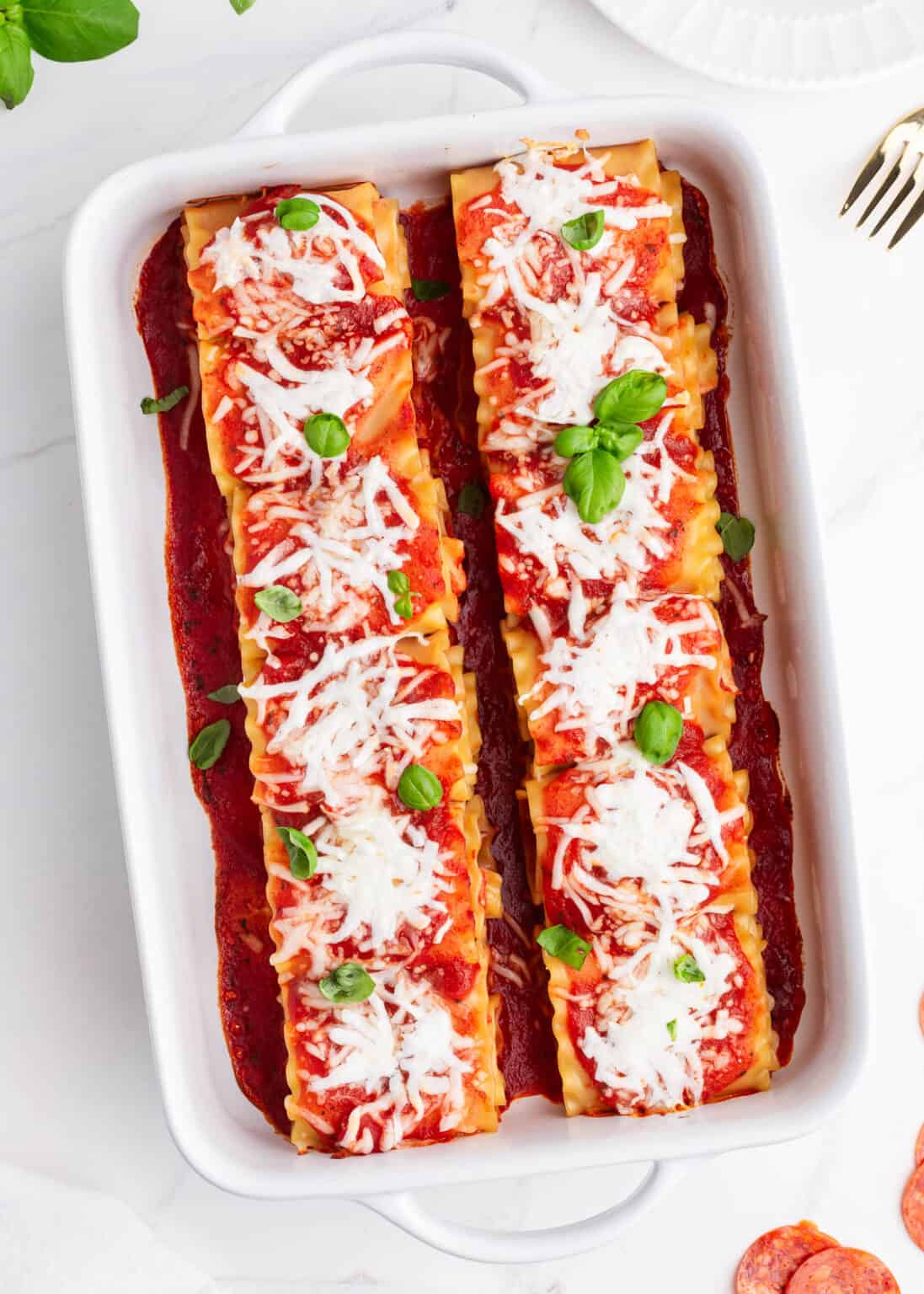 Pepperoni lasagna roll ups in a white baking dish.