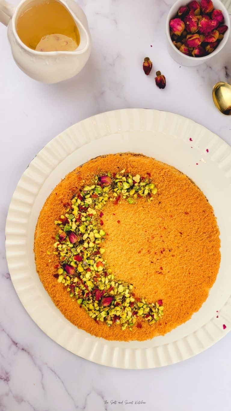 Knafeh, phyllo dough and cheese dessert, on a white plate with ingredients in the background.