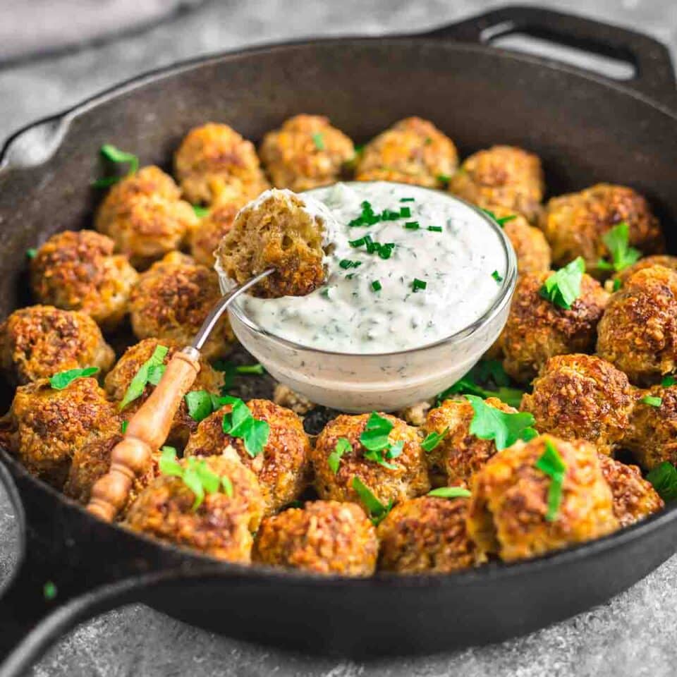 Keto sausage balls with dipping sauce in a cast iron pan.