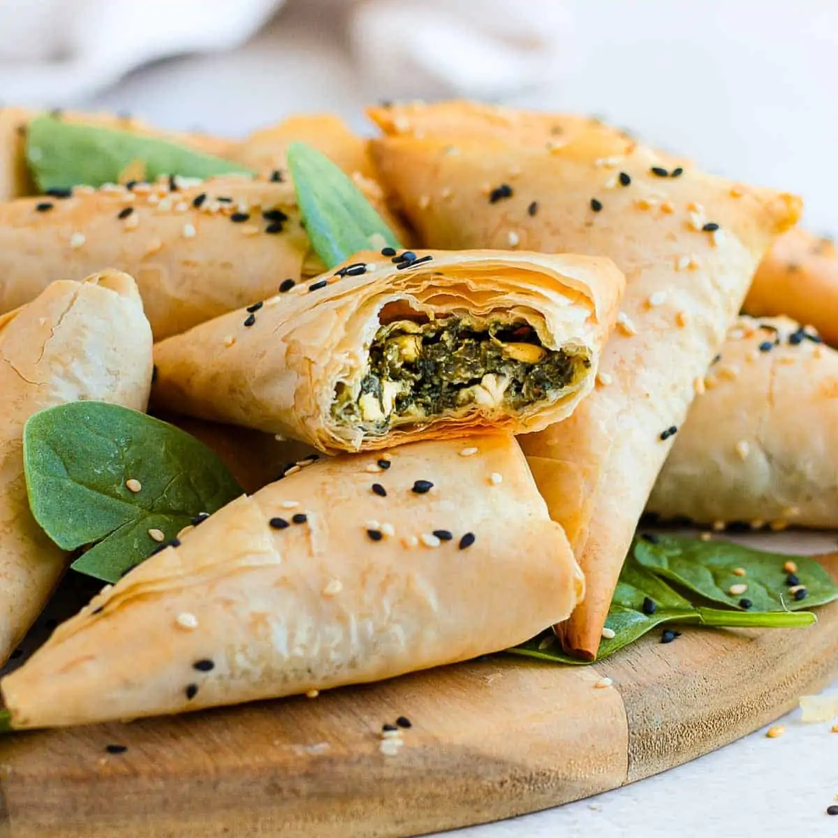 Spinach and feta triangles stacked atop one another on a wooden board.