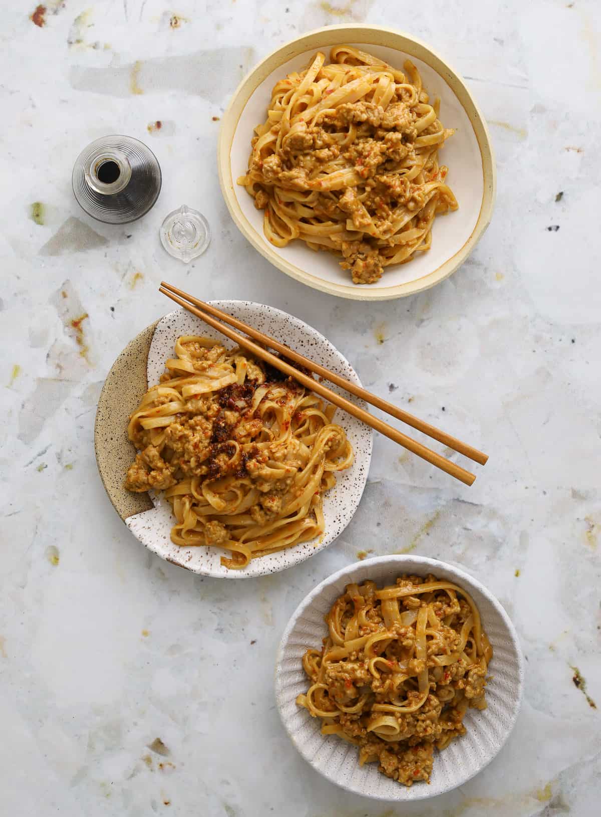 5 Ingredient spicy pork and peanut noodles on plates with chopsticks.