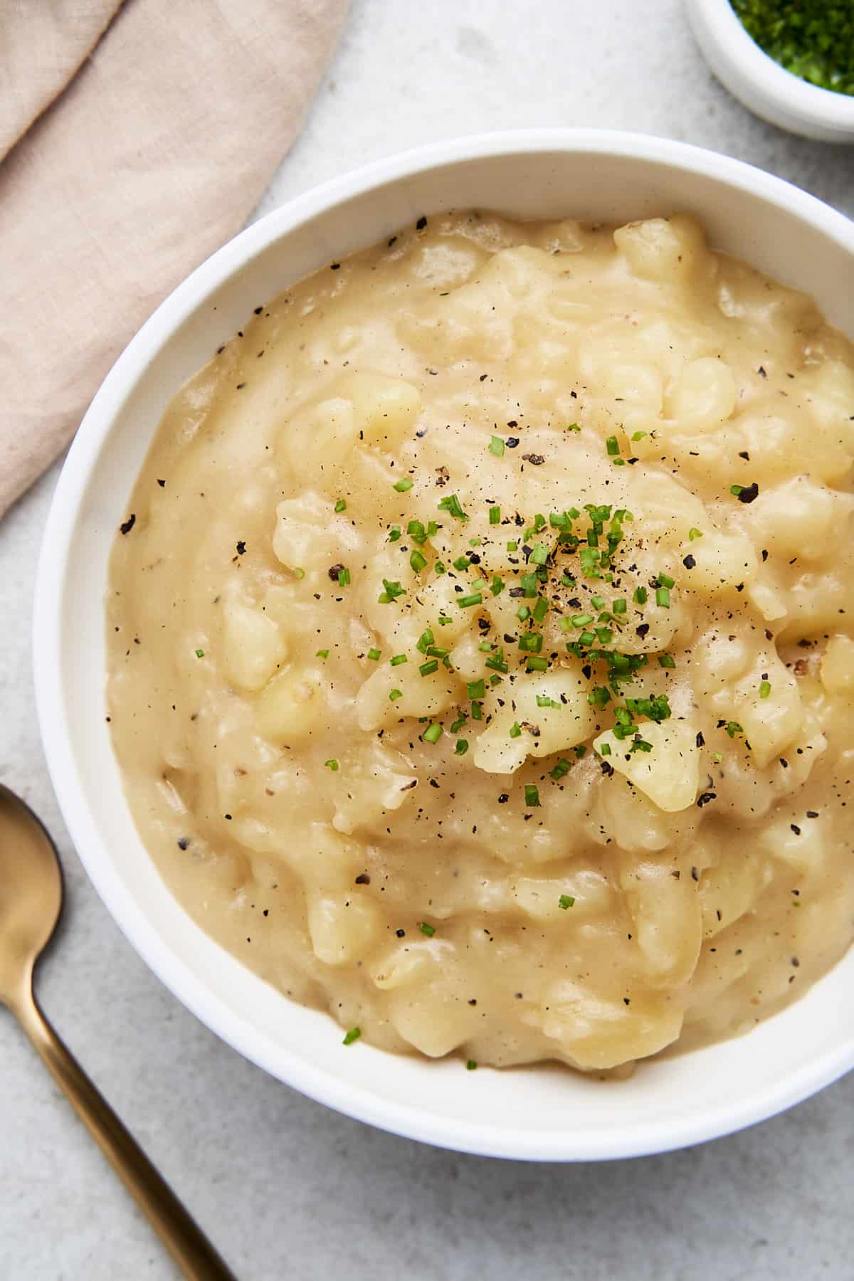 Bowl full of stewed potatoes with chives and black pepper.