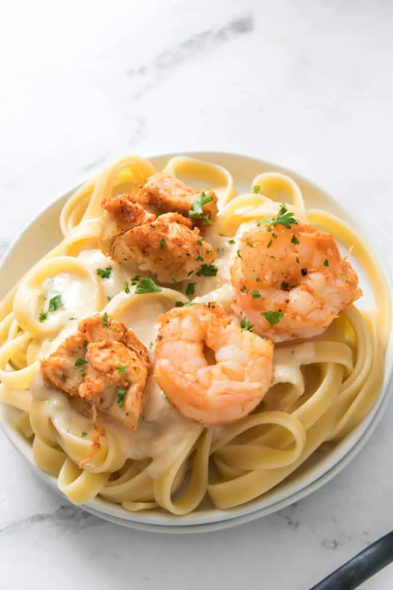 Cajun seasoned chicken and shrimp atop alfredo sauce and noodles on a white plate.