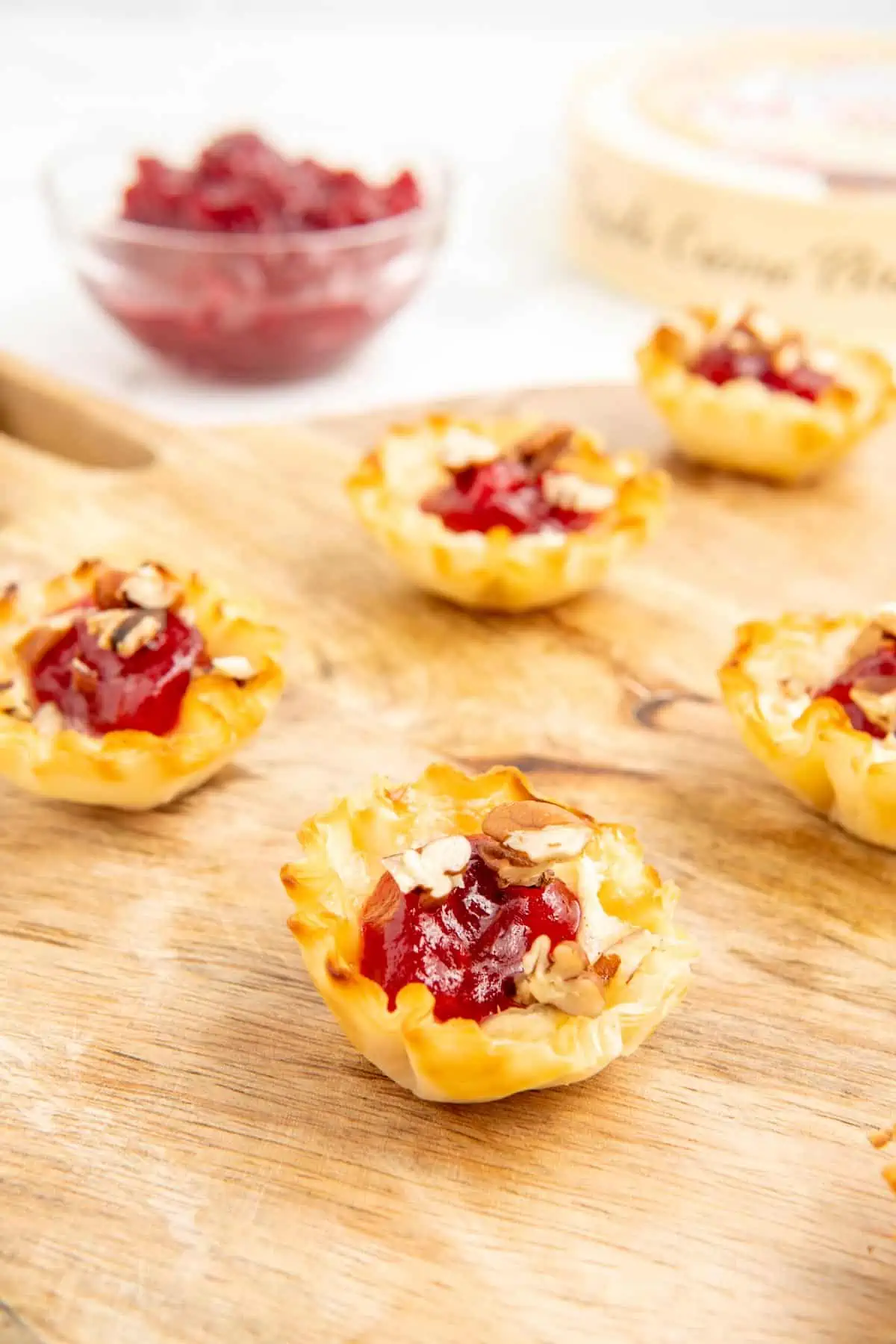 Phyllo shells filled with brie cheese, cranberry sauce, and pecans on a wooden surface.
