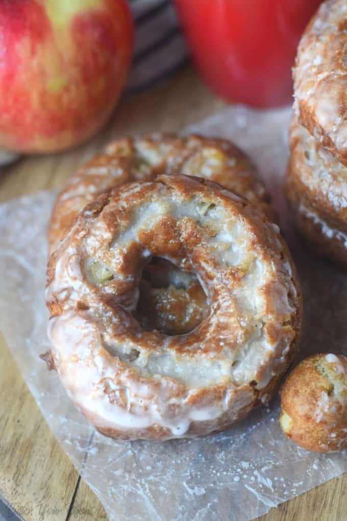 Stack of apple cider donuts with apples in the background.