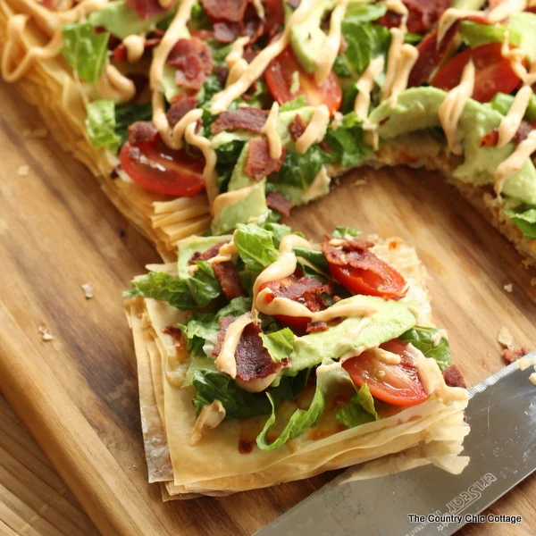 Avocado BLT pizza with a slice removed on a wooden cutting board and knife.