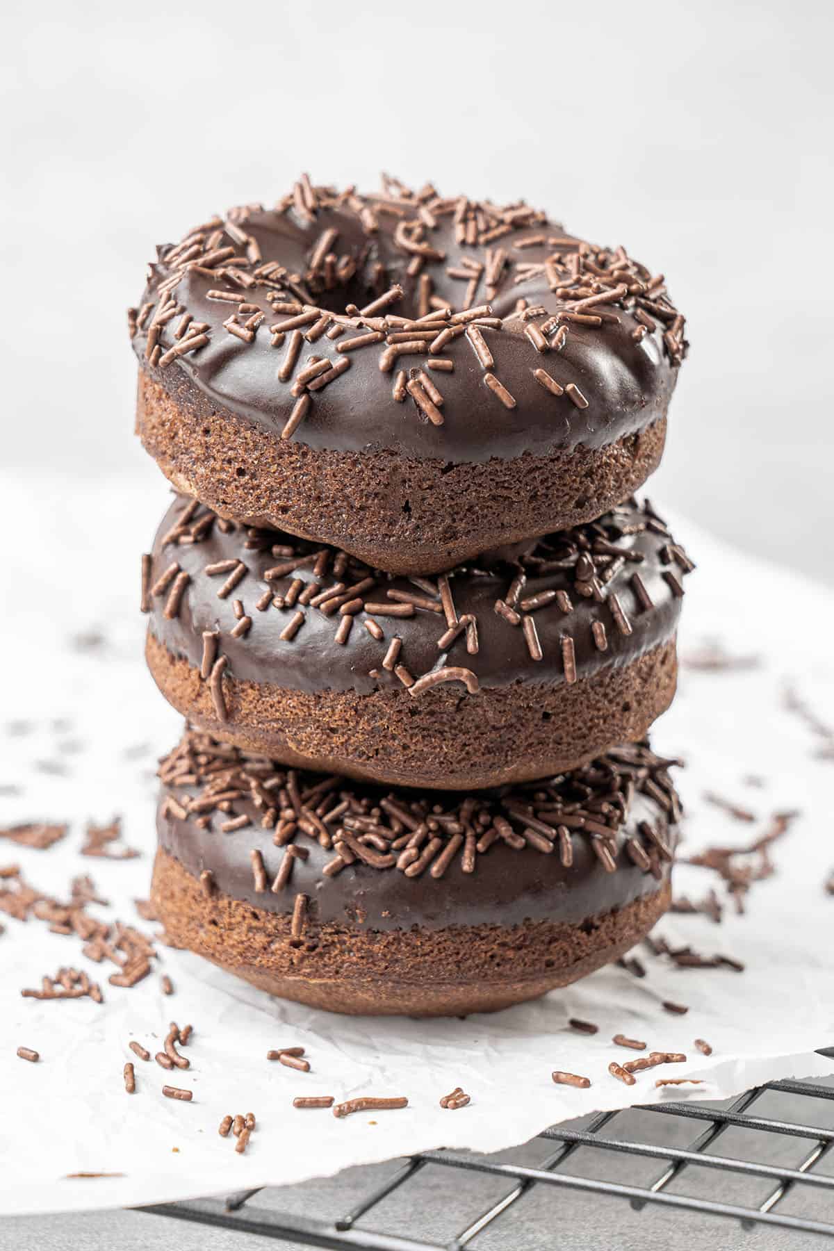 Stack of baked chocolate donuts with chocolate glaze and sprinkles.