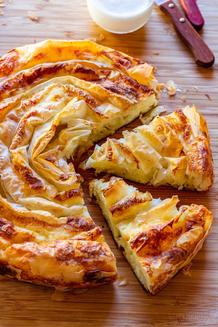 Traditional Bulgarian cheese pie on a wooden cutting board with slices separated.