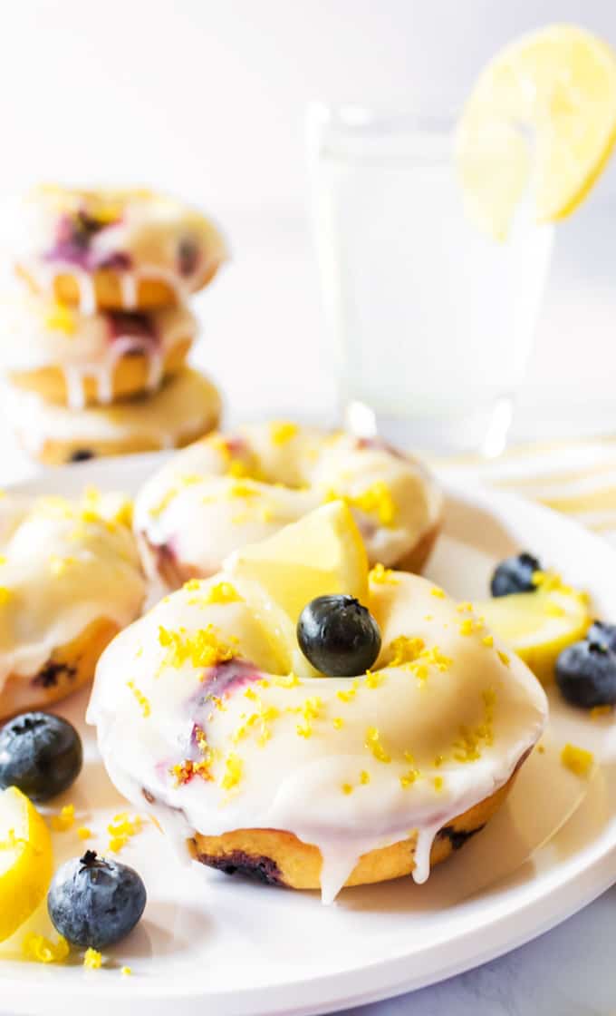 Blueberry donuts with glaze, lemon zest, fresh blueberries, and lemon slice.