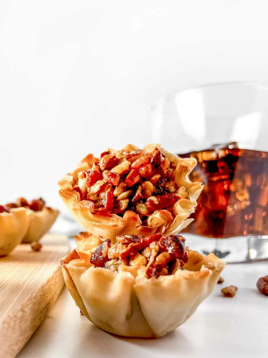 Bourbon pecan pie bites stacked with glass of bourbon in the background.