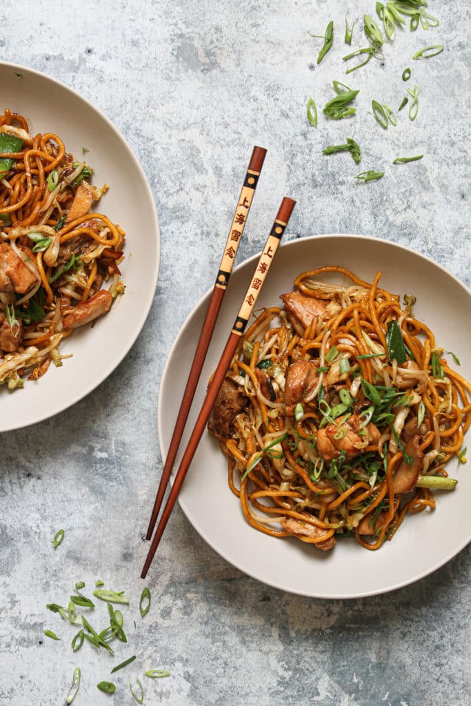 Chicken chow mein served on white plates with chopsticks.