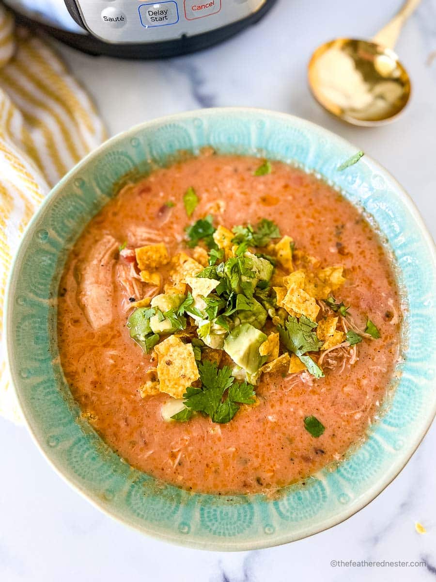 Instant Pot tortilla soup serving in a decorative turquoise bowl with the pressure cooker in the background.