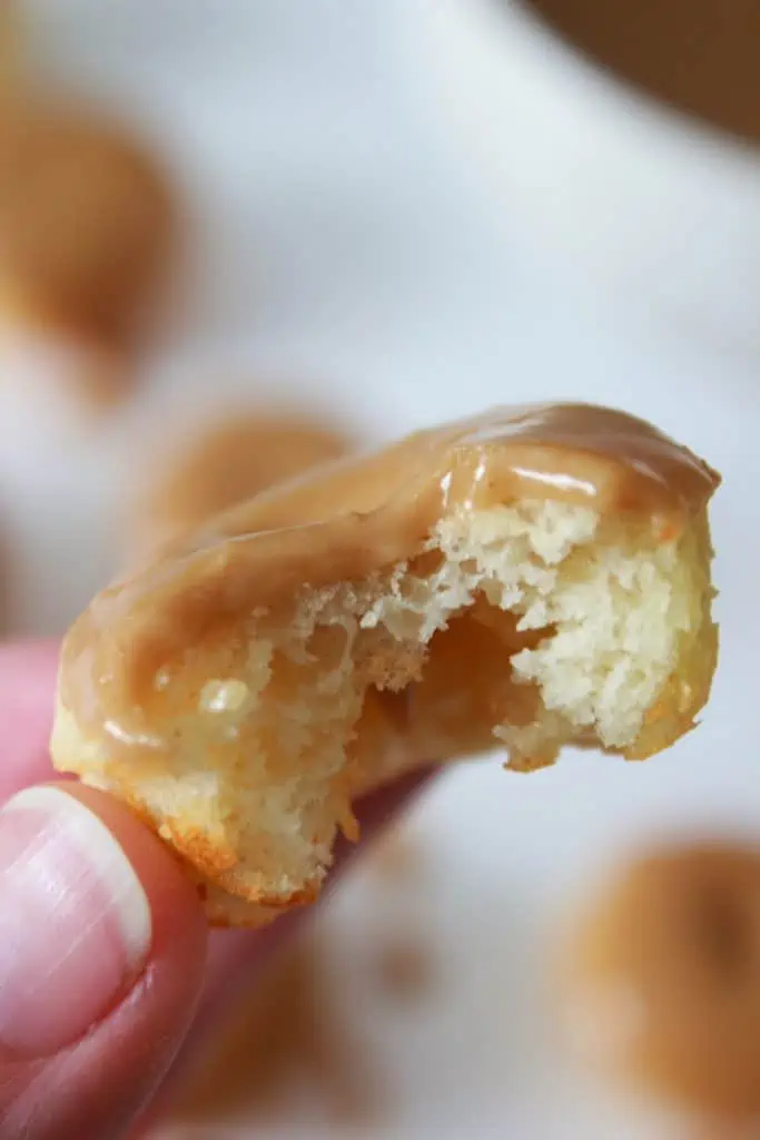 Hand holding mini pancake donut with bite taken out.