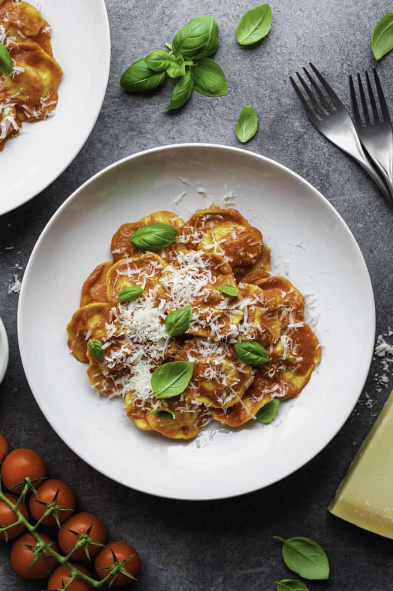 Ravioli Al Pomodoro on a white plate with forks and basil in the background.