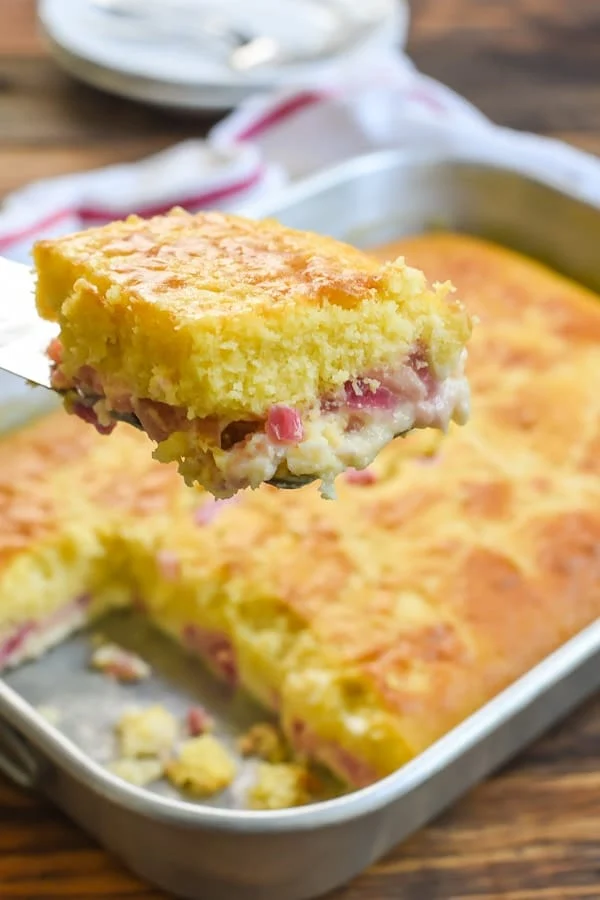 Slice of easy rhubarb custard cake with rest of cake in the background.