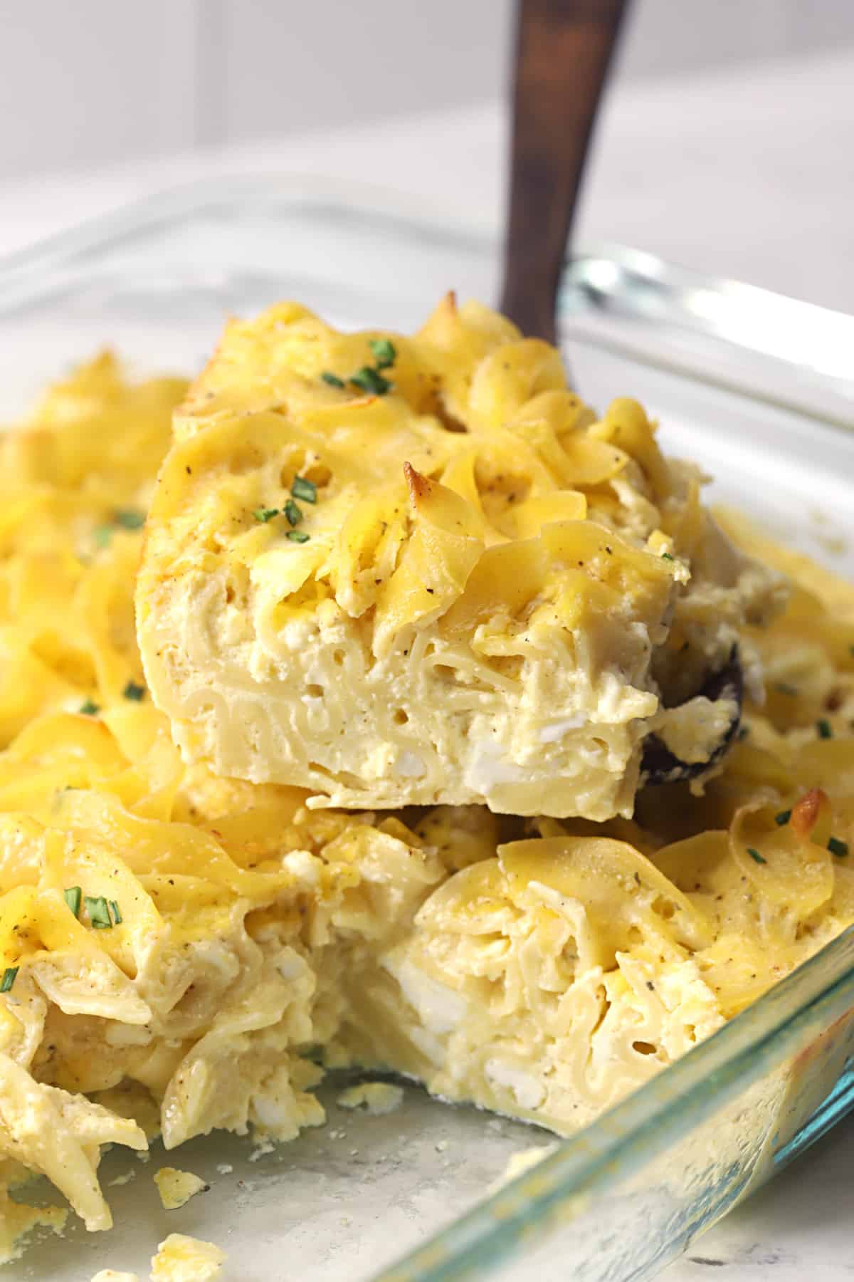 Brown butter noodle kugel being scooped with a wooden spoon.