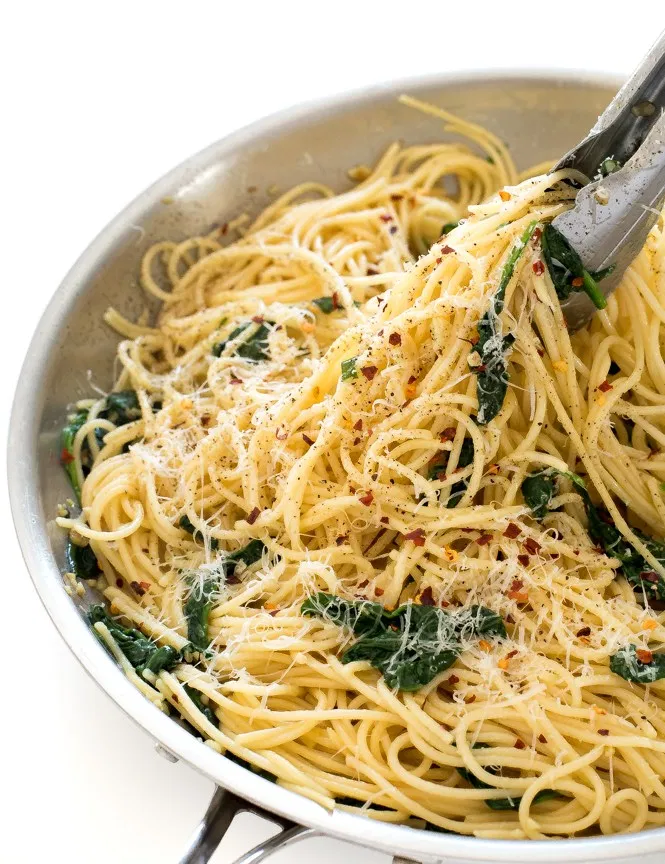 Pasta with garlic, spinach, and cheese pulled with tongs in a pan.