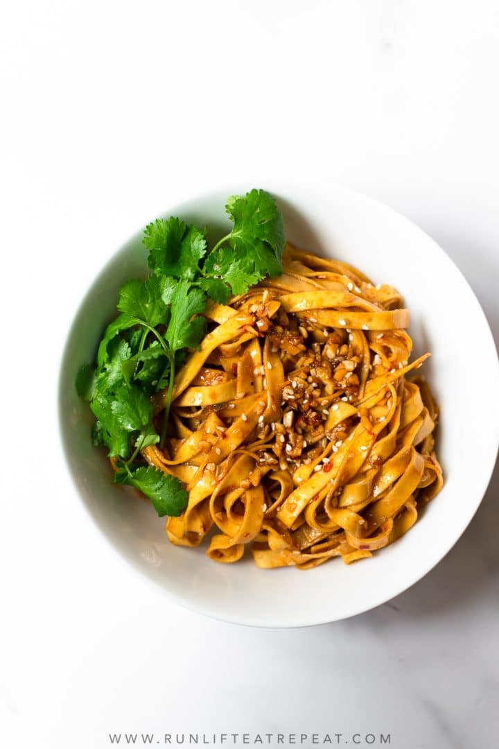 Bowl of saucy noodles with cilantro on an all white background.