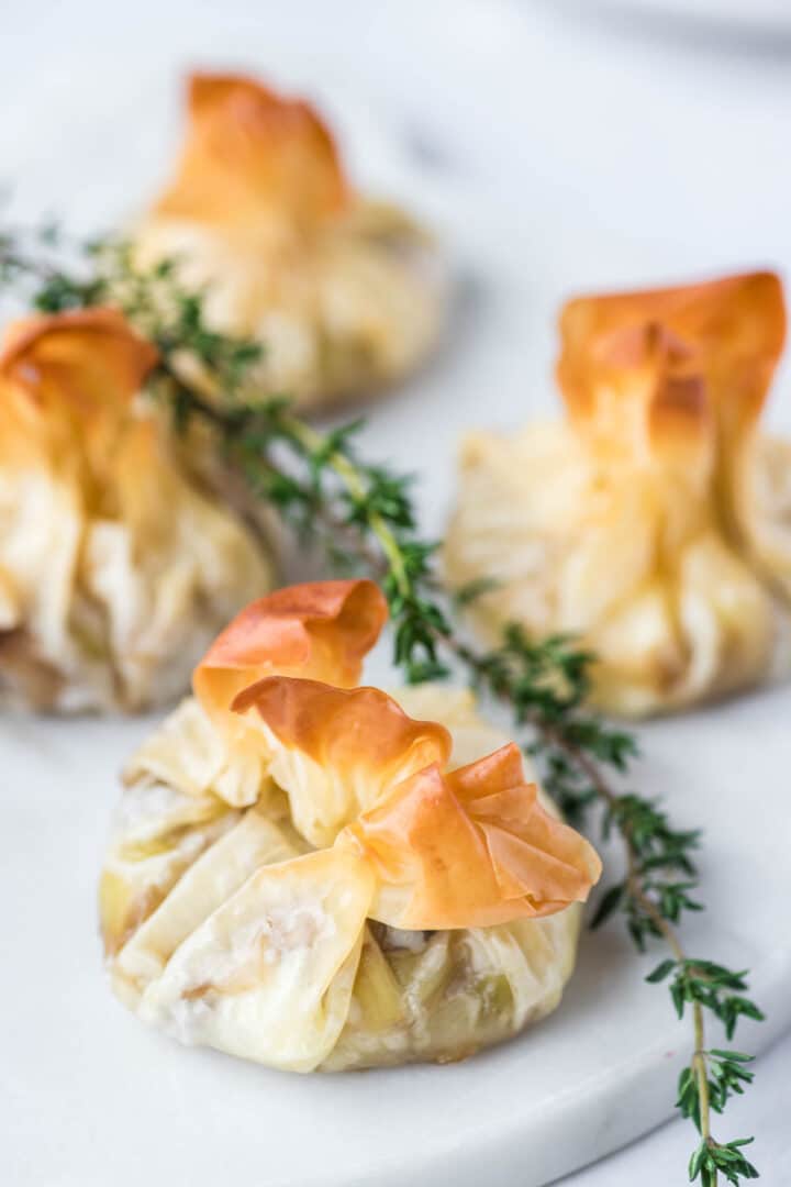 Mushroom goat cheese filo pastry parcels with thyme sprigs on a white plate.