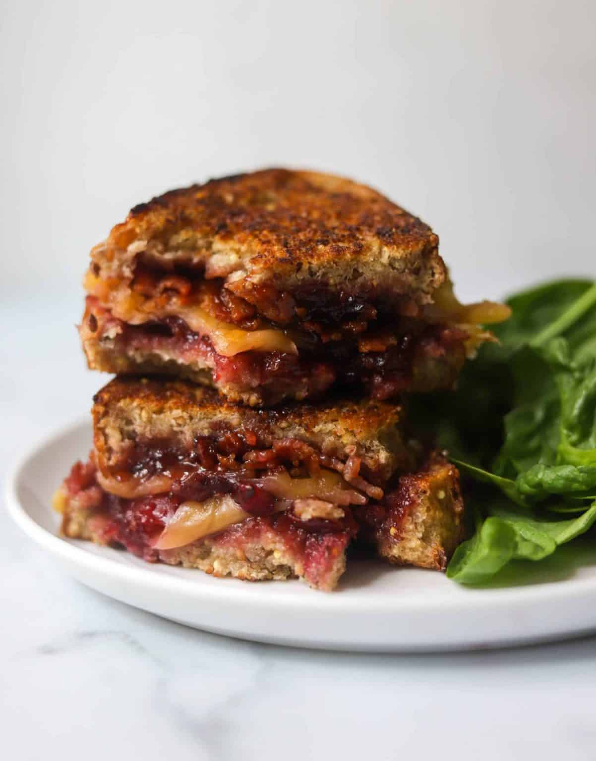 Cherry bacon grilled cheese on a plate with basil on a white plate.