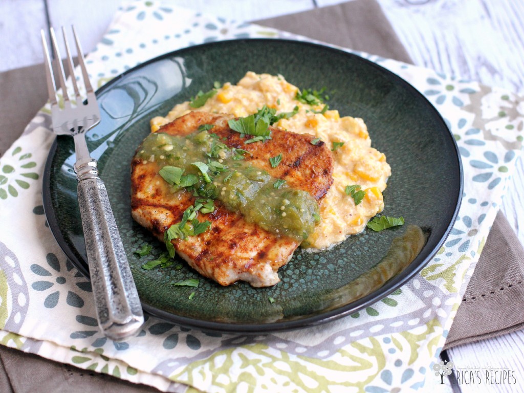 Coffee rubbed pork chop on top of creamy cheese corn on a bluish plate with a fork.