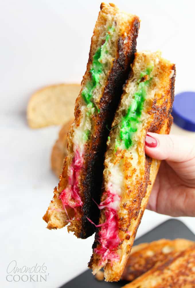 Festive grilled cheese with green and red dyed mozzarella cheese held in hand.