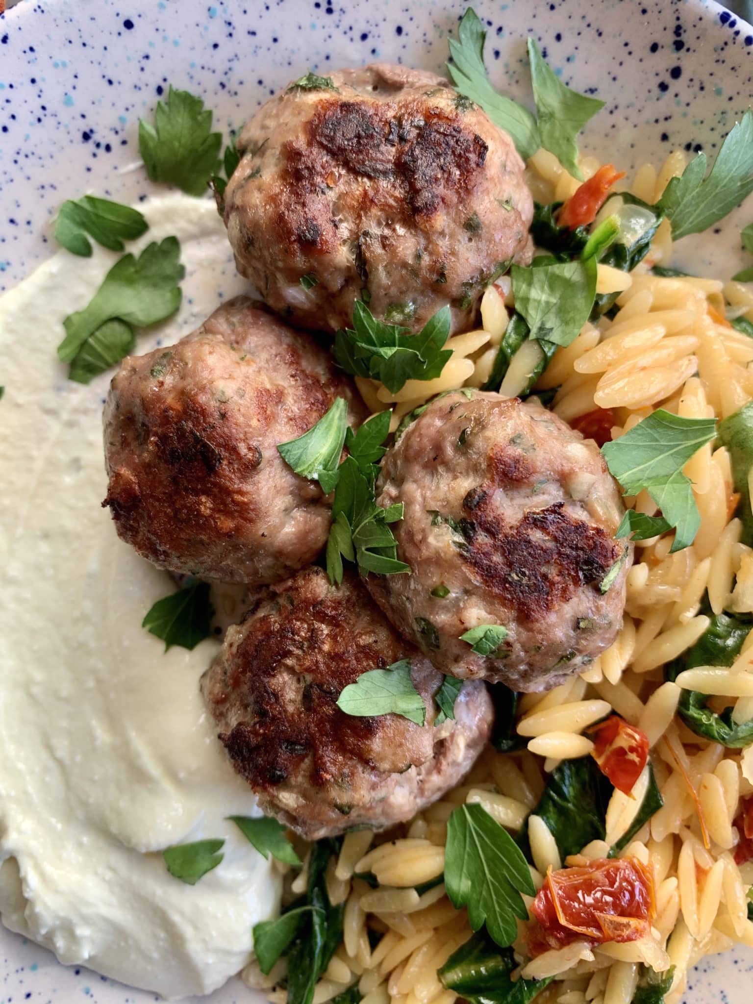 Greek meatballs with colorful sun-dried tomato orzo and whipped feta on a plate.