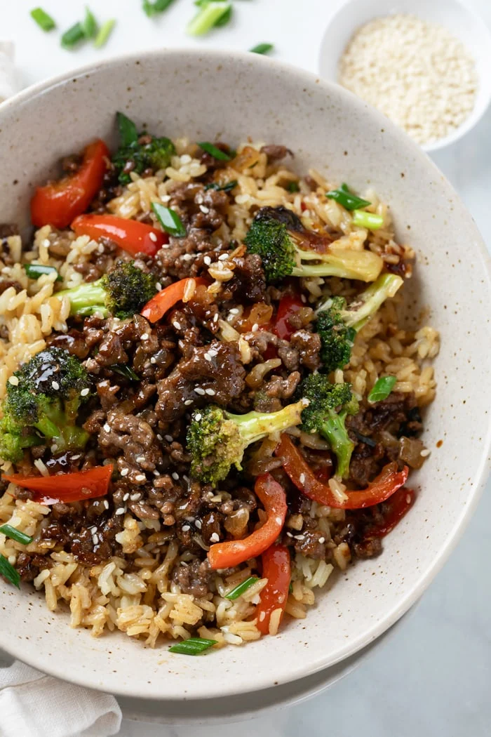 Ground beef and broccoli with rice in a white bowl on a white background.