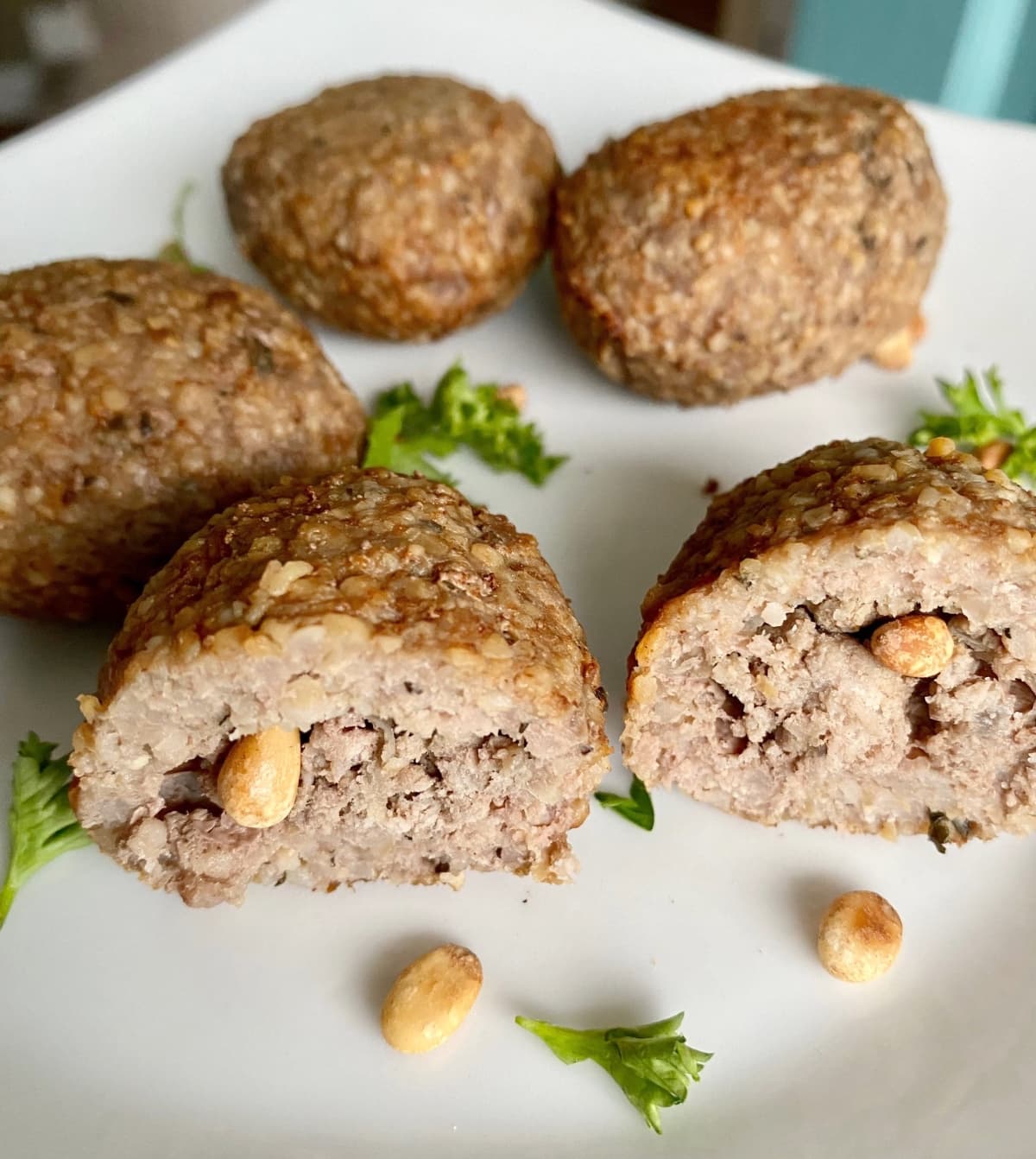 Kibbeh balls with pine nuts on a white plate.