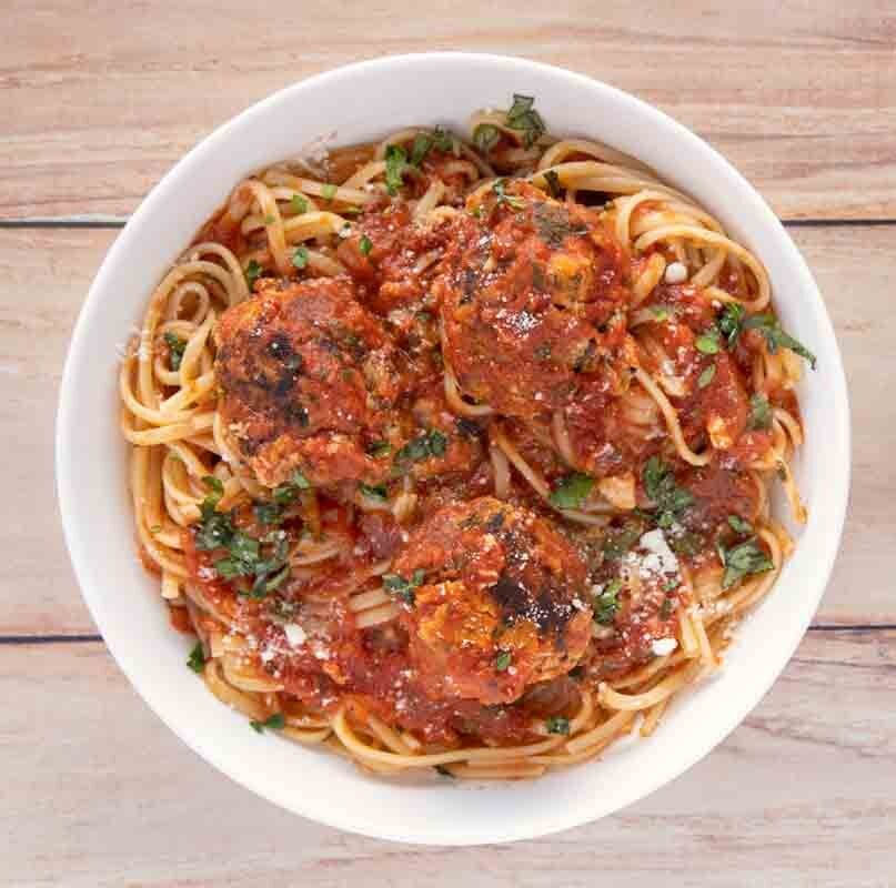 Tuna meatballs with linguine in a white bowl on a wooden board.