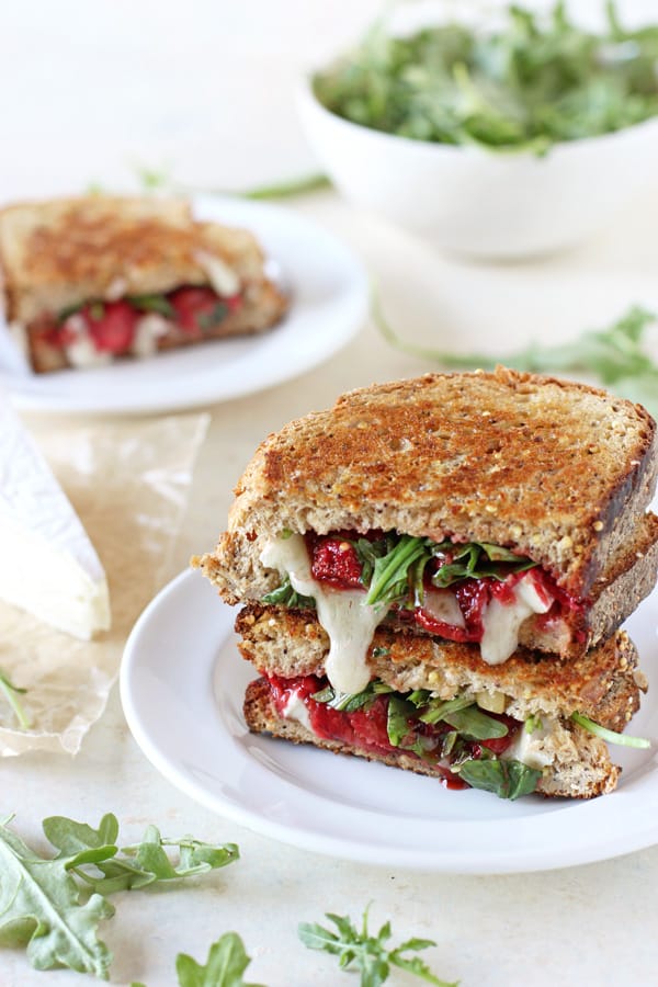 Roasted strawberry, arugula, and brie grilled cheese sandwich cut in half on a plate.