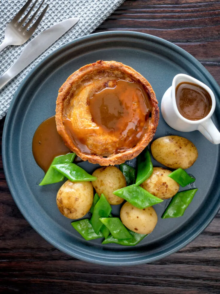 Homemade Scotch pie with lamb on a blue plate with gravy, potatoes, and snow peas.