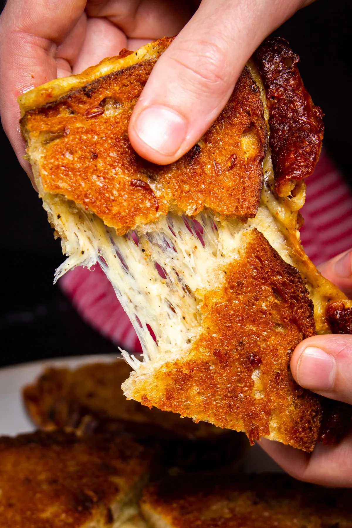 Hands holding grilled cheese sandwich, tearing it half showing cheese pull.