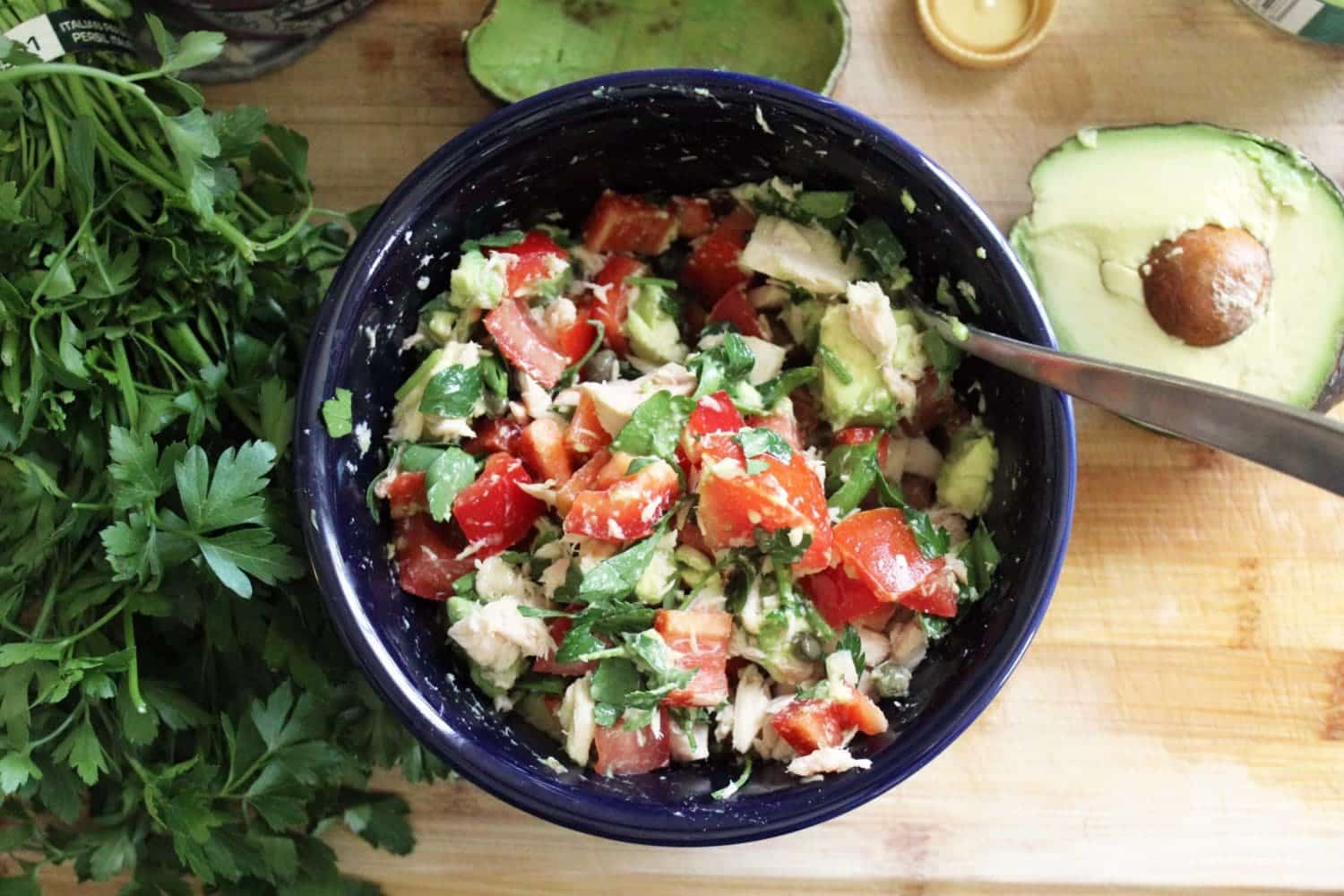 Spanish tuna salad with avocado in a blue bowl with ingredients around.