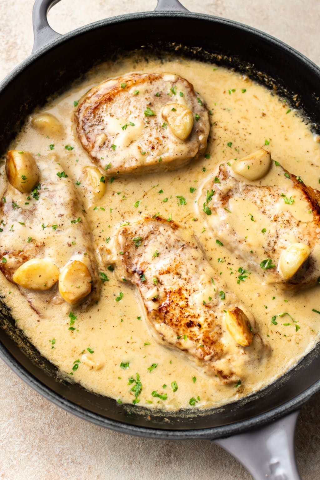 Pork chops with garlic and cream sauce in a cast iron pan.