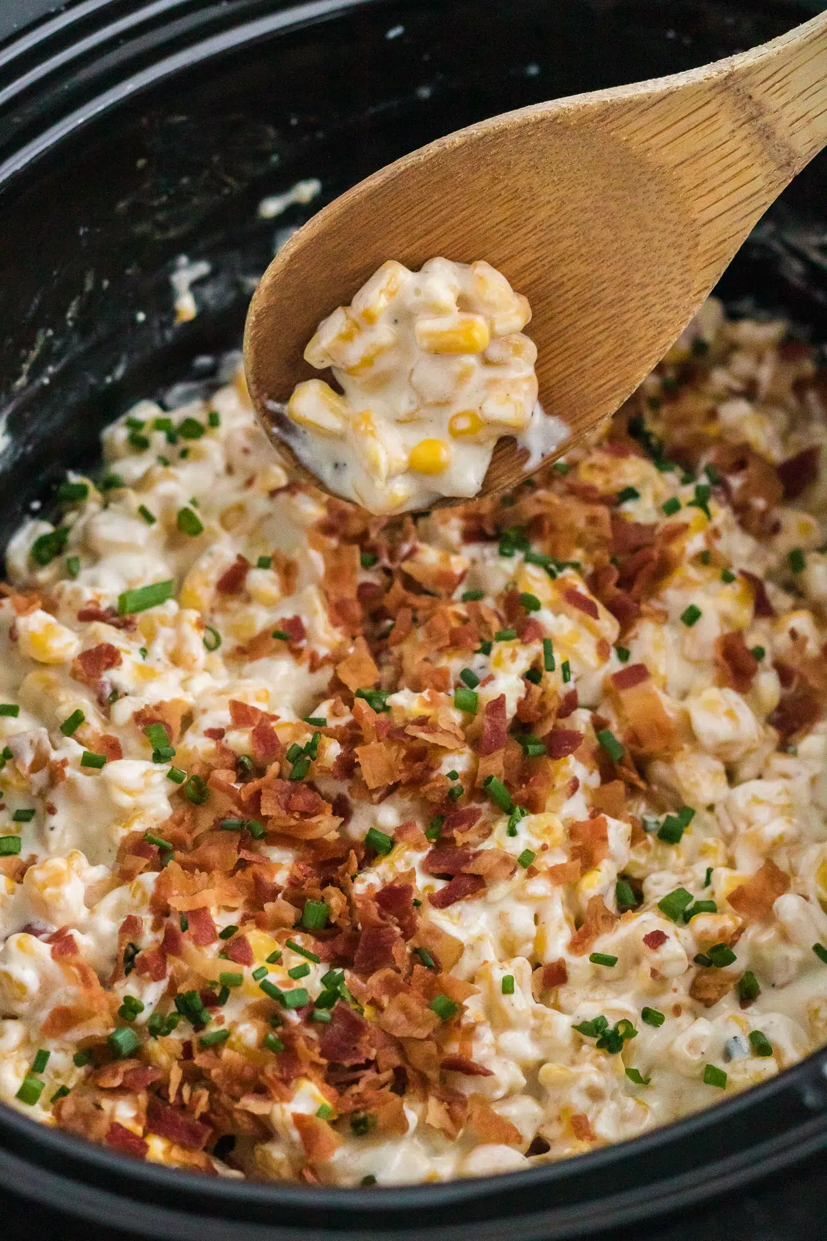 Spoon scooping some creamed corn in a slow cooker.