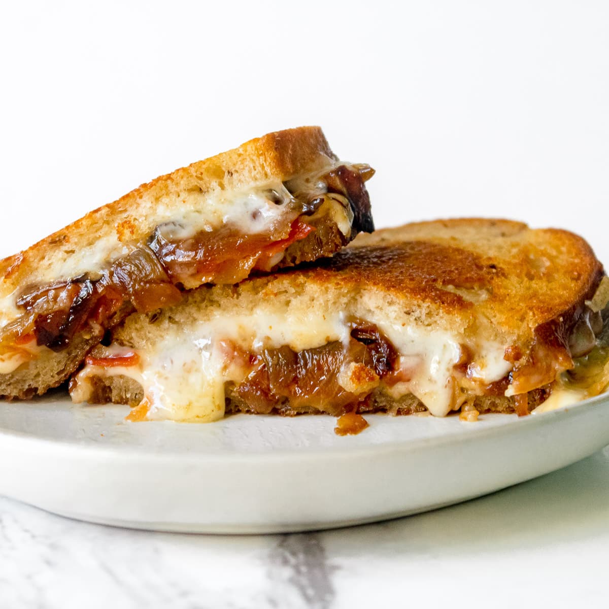 Havarti Grilled cheese with bacon and caramelized onion on a plate with white background.