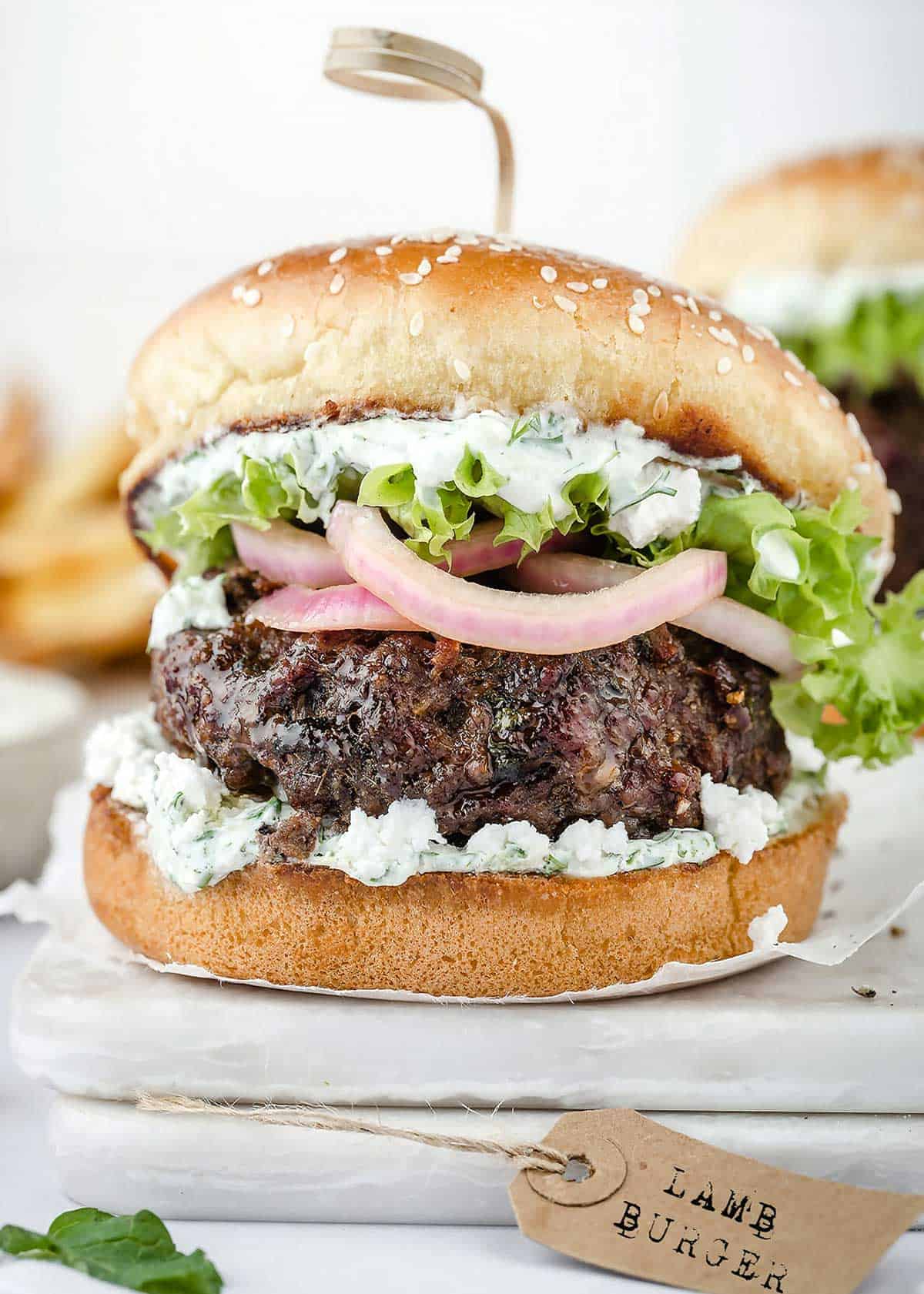 Juicy lamb burger on a bun with tzatziki, feta, lettuce, and pickled red onions.