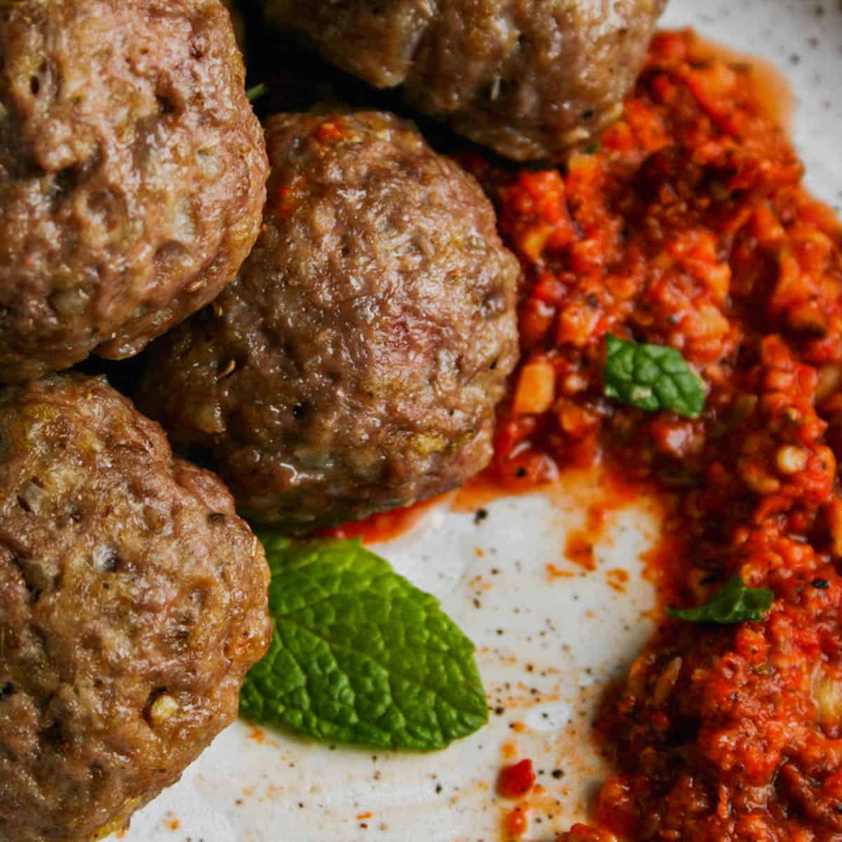 Juicy lamb meatballs on a white plate with Middle Eastern inspired Romesco sauce.