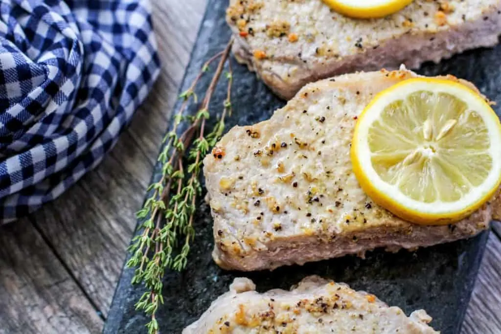 Lemon pepper pork chops with lemon slices on a piece of slate.