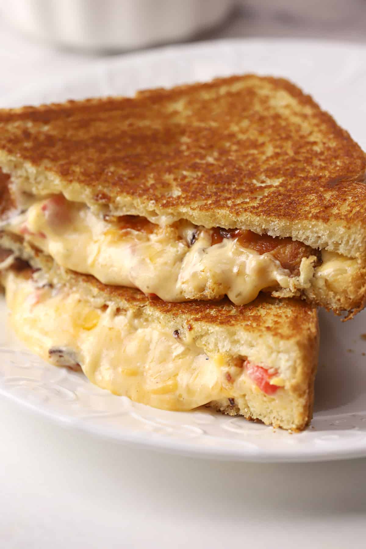 Golden brown bacon pimiento grilled cheese cut in half on a white plate.