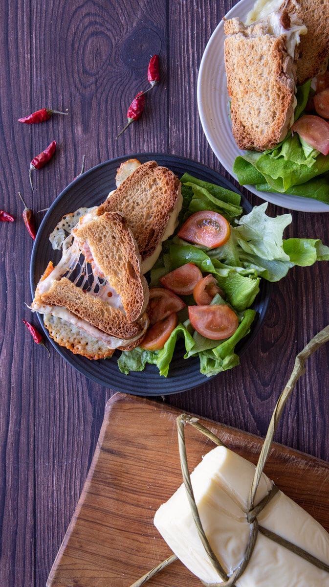 Provola and nduja on a plate with lettuce and tomatoes and more in the background.