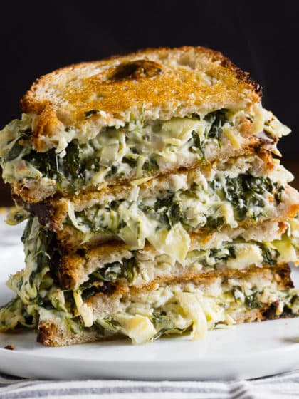 Spinach and artichoke dip grilled cheese cut in half and stacked on a plate.