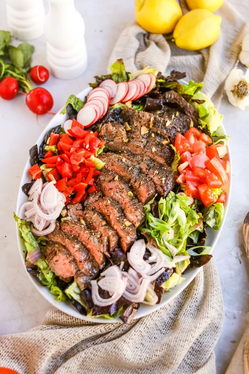 Colorful flank steak salad with balsamic dressing with sliced radishes, diced tomatoes, red onions, and diced bell peppers on a bed of lettuce.