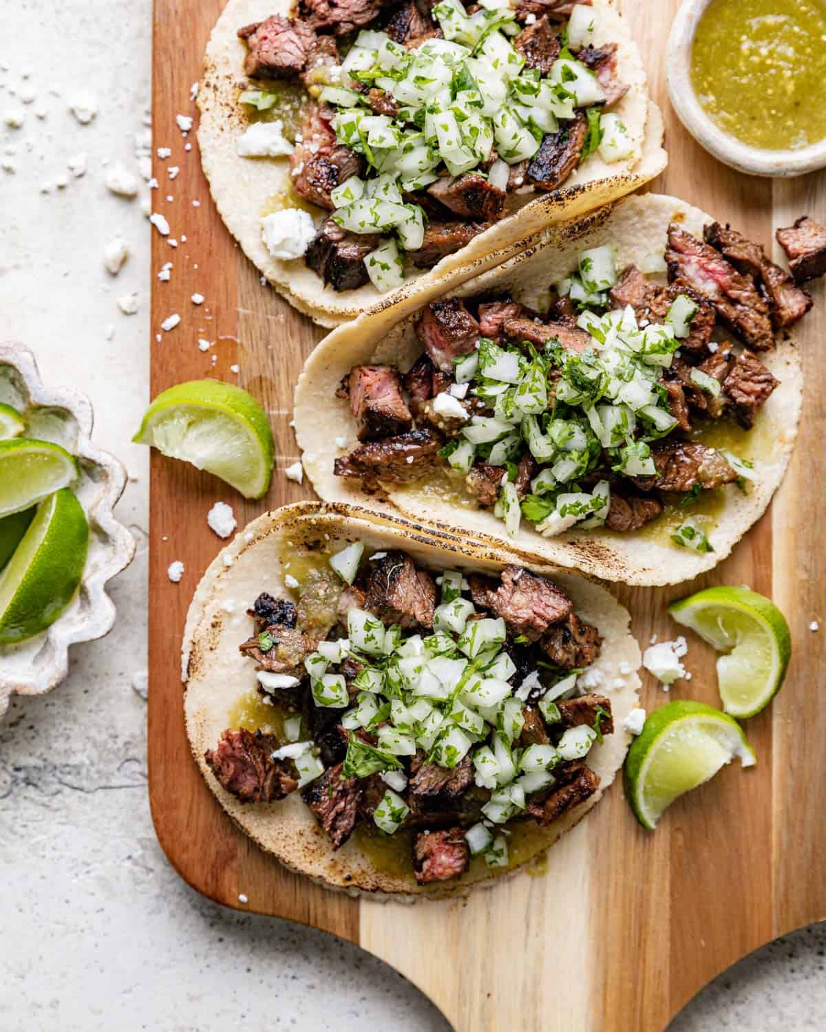 Steak street tacos with onions and cilantro on a wooden cutting board.