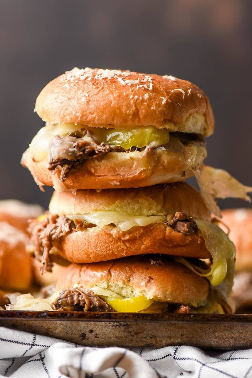 Stack of pulled roast beef sliders with cheese and peppers.