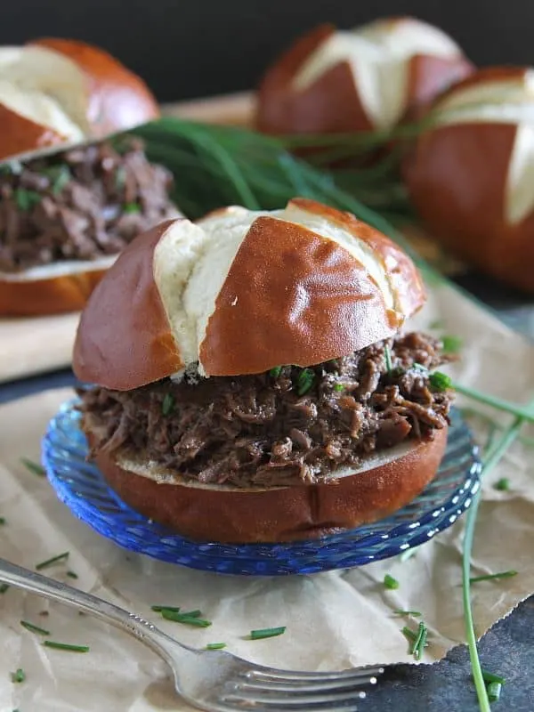 Cherry beef carnitas sandwiches on pretzel rolls on a blue saucer.