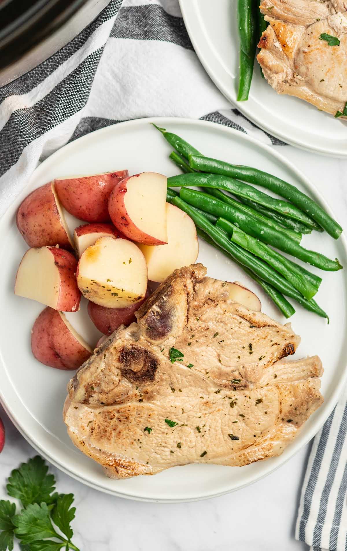 Slow cooker ranch pork chops on a plate with red potatoes and green beans on a white plate.