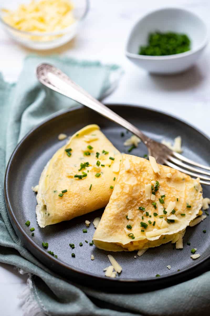 Two crepes filled with cheesy eggs and topped with chives and shredded cheese.